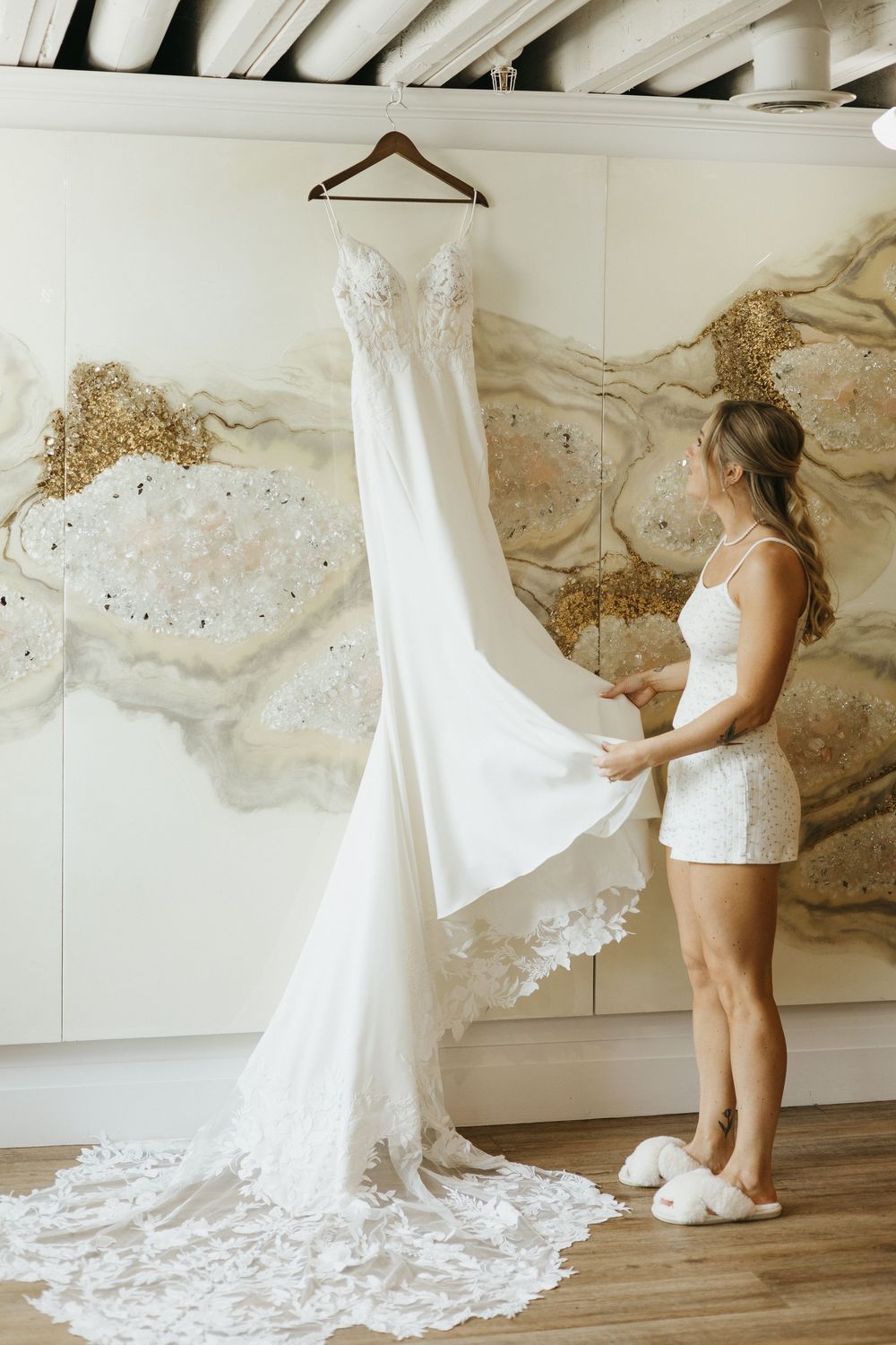 A wedding dress is being hung and arranged in an art gallery with neutral walls and abstract paintings at Timberbarn St Jacobs
