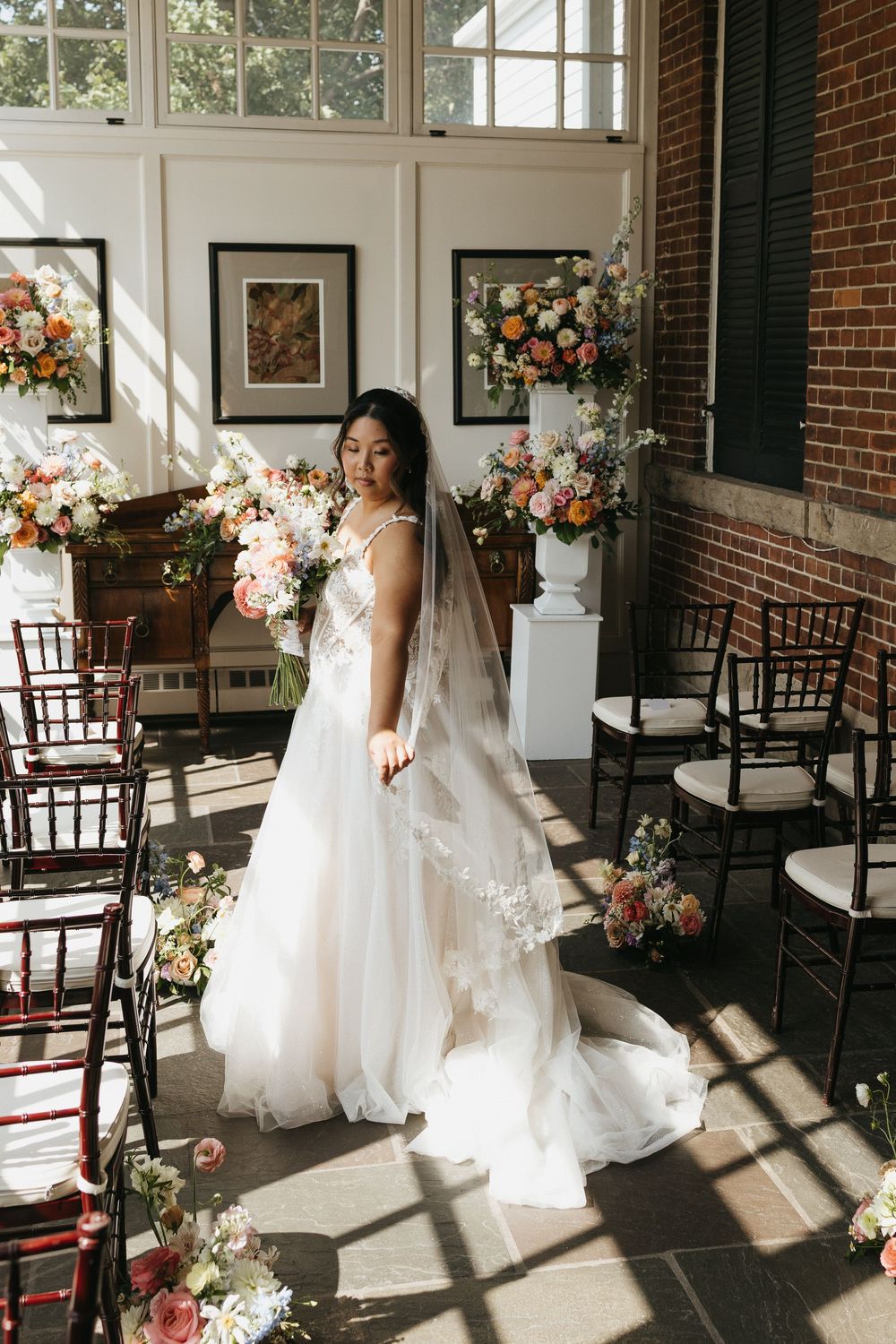 Sunlit indoor wedding venue with wooden chairs, exposed brick walls, and floral arrangements creating romantic shadows at Langdon Hall