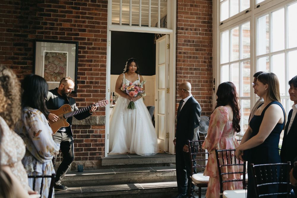 A wedding party gathers in a rustic brick-walled venue with large windows and natural light at Langdon Hall in Cambridge Ontario