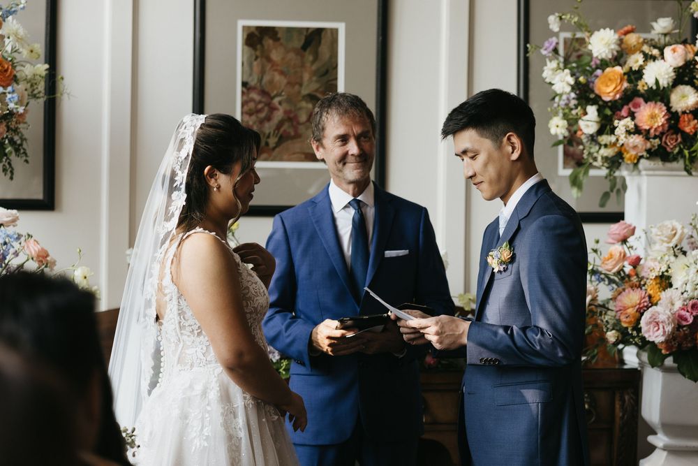 A couple shares an intimate moment during their wedding ceremony surrounded by floral arrangements and elegant decor at Langdon Hall