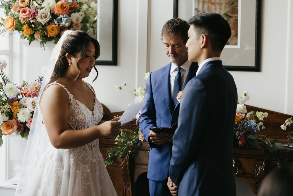 Wedding party members gather in a bright indoor venue decorated with orange and peach floral arrangements at Langdon Hall