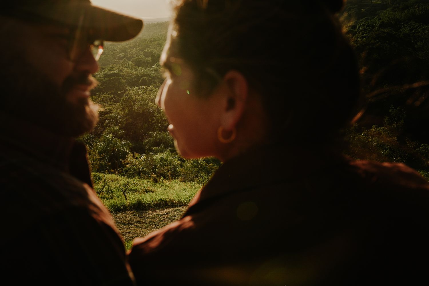 Couple sharing an intimate moment outdoors with lush green hills in warm golden sunset light.