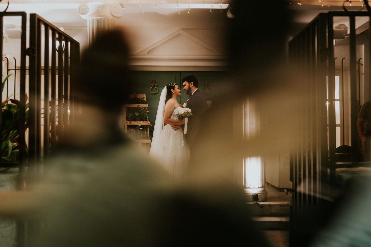 A couple shares a romantic first kiss at the altar during their elegant indoor wedding ceremony.