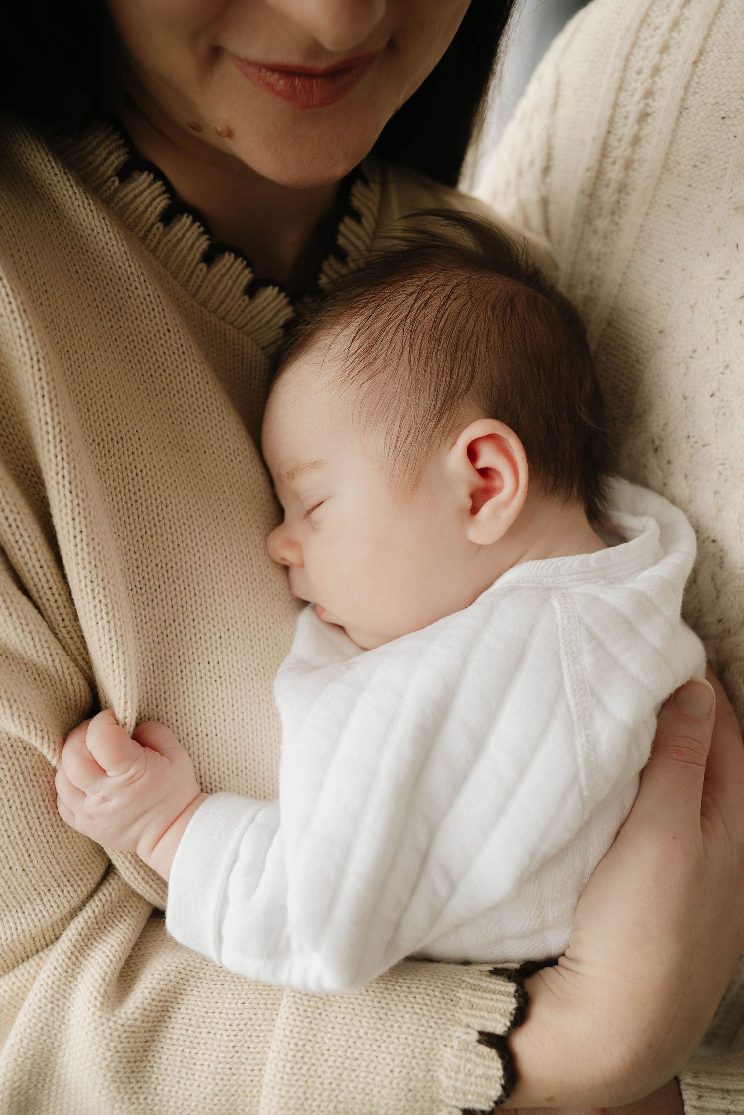A sleeping baby wearing a cozy cream-colored knit romper lies peacefully on soft fabric.