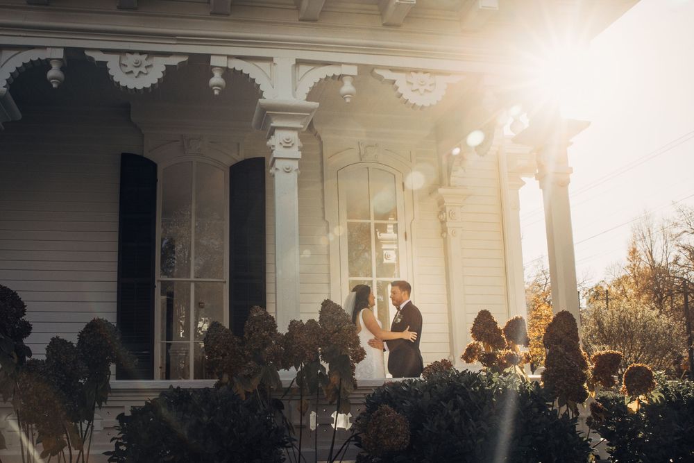 Couple stands in golden sunlight during outdoor New England wedding ceremony with guests seated in background shot by Justin Potter