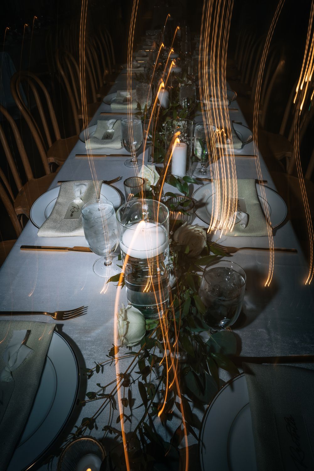 Elegant table settings with white linens, wine glasses, and rustic wooden decor elements illuminated in warm lighting.