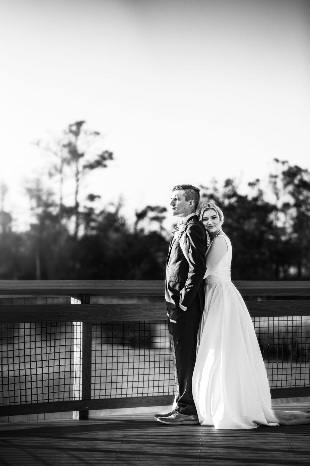 Black and white wedding portrait on wooden deck with dramatic lighting and shadows.