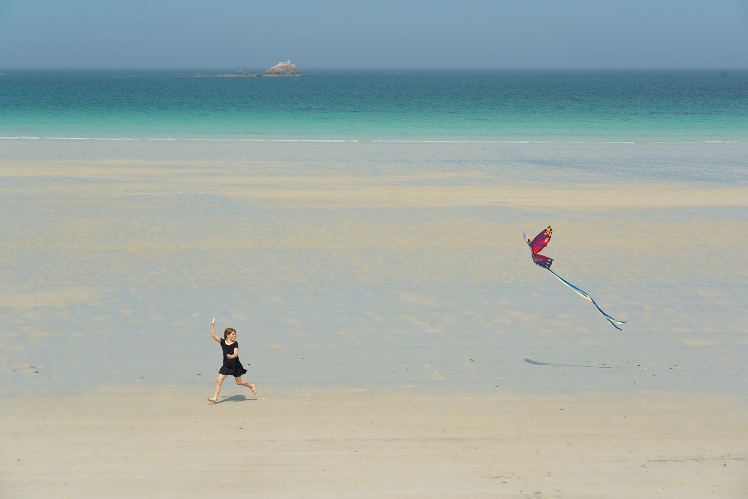 Watersports activities and colorful kites flying over a pristine turquoise ocean beach with clear blue sky.