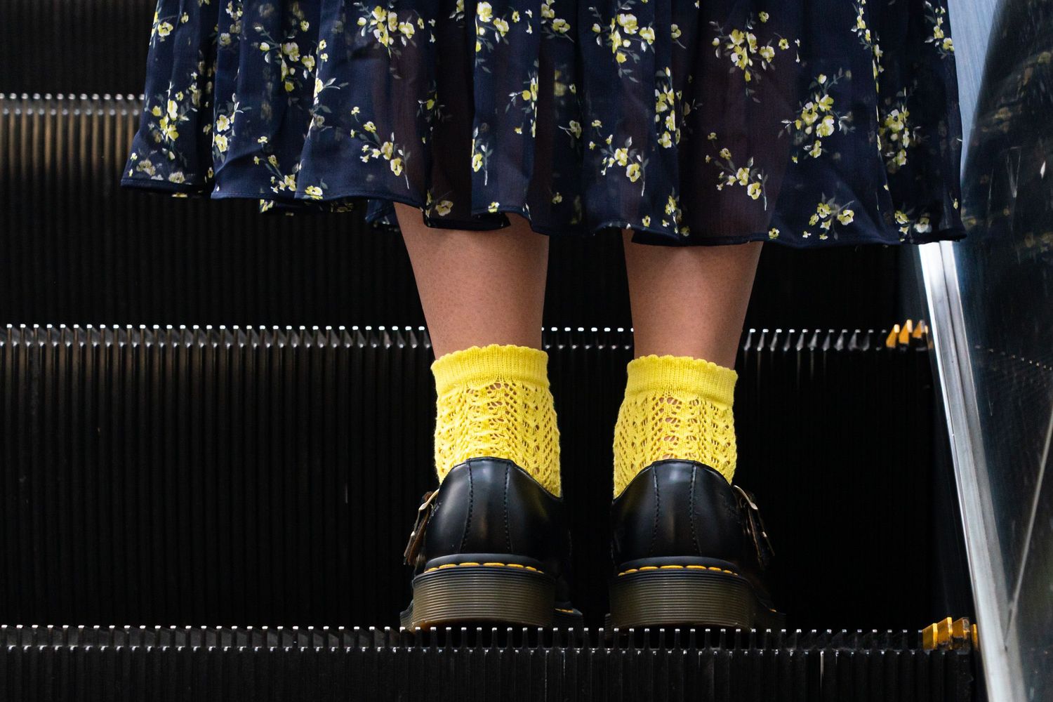 Yellow socks worn with black boots against a dark background and reflective flooring surface.