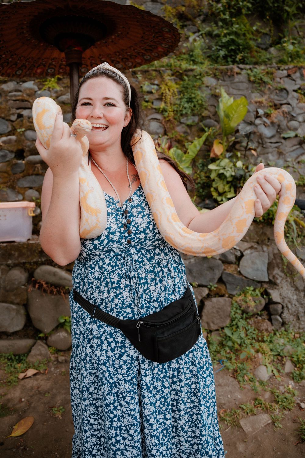 Woman in floral dress holding a large albino snake while smiling outdoors.
