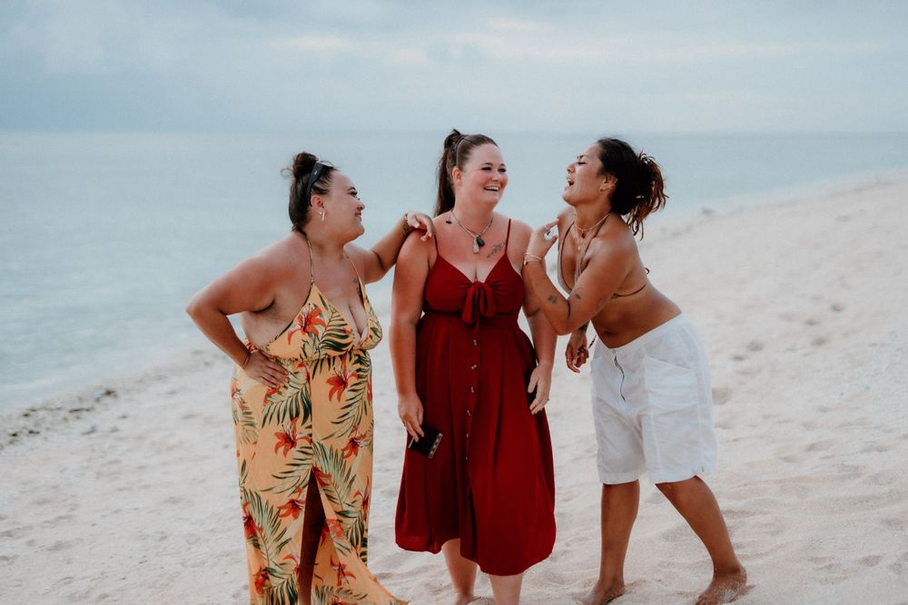 Three friends laughing together on a sunny beach.