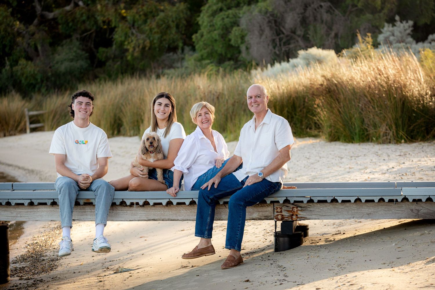 Family group sitting together on wooden deck at sunset with their dog.