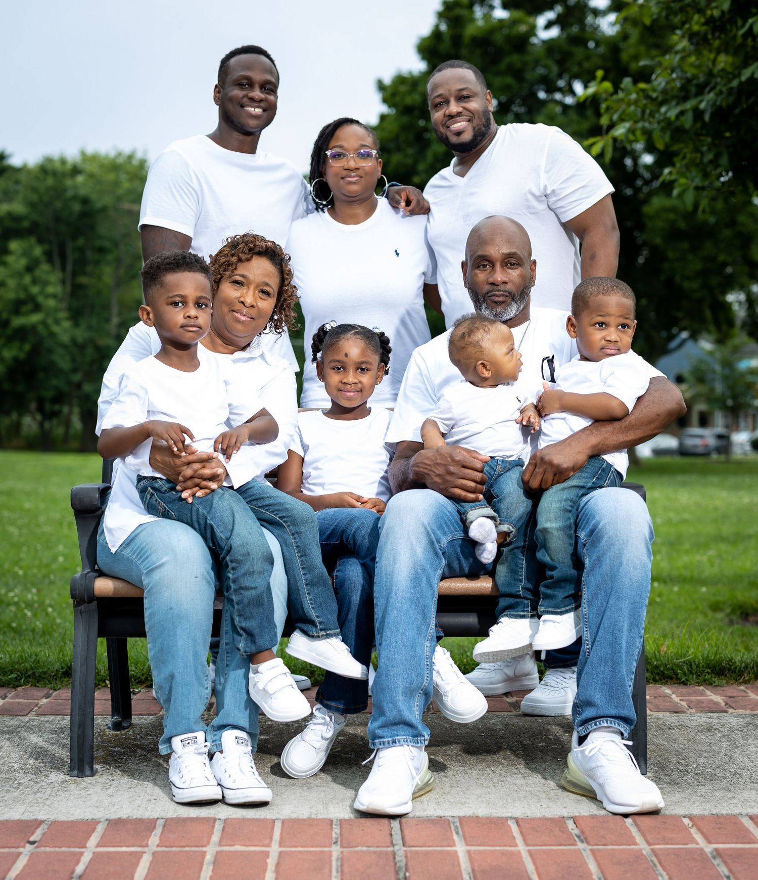 Multi-generational family in white shirts sitting together on outdoor bench.