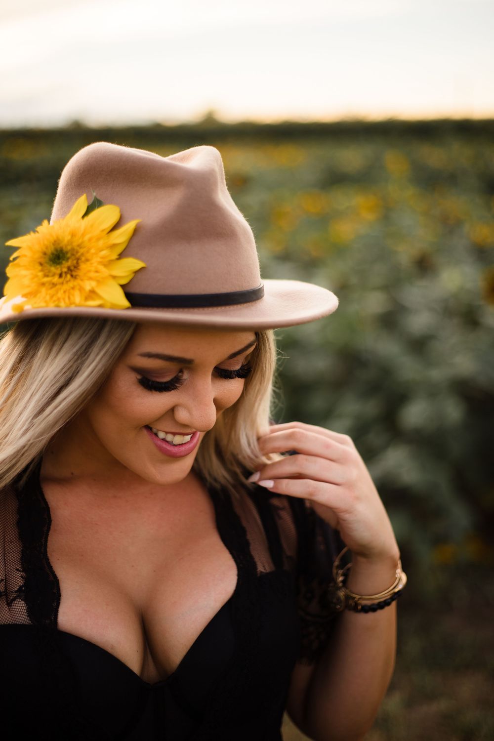 Woman in black dress and beige hat posing in a sunflower field at sunset.