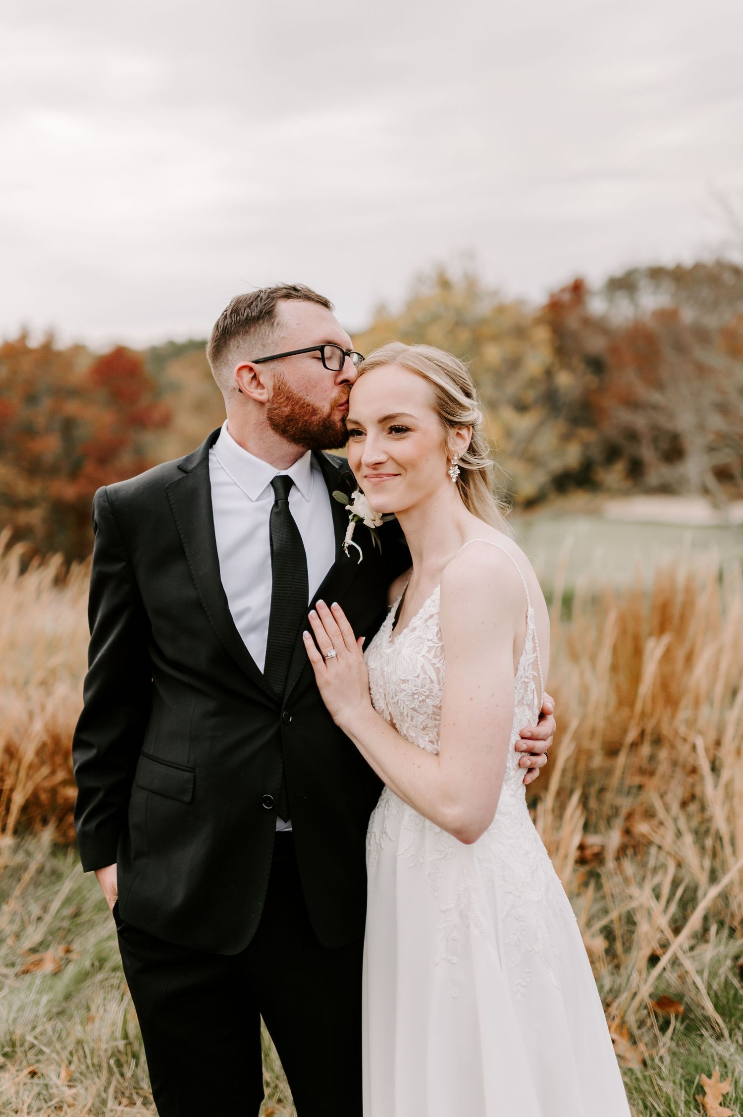 A wedding couple poses together against a backdrop of autumn colors and tall grass.
