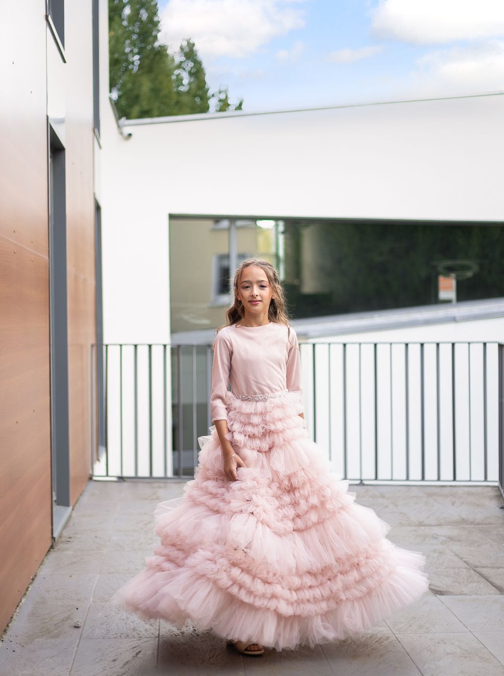 Young person twirling in a luxurious pink tulle ballgown on an outdoor terrace.