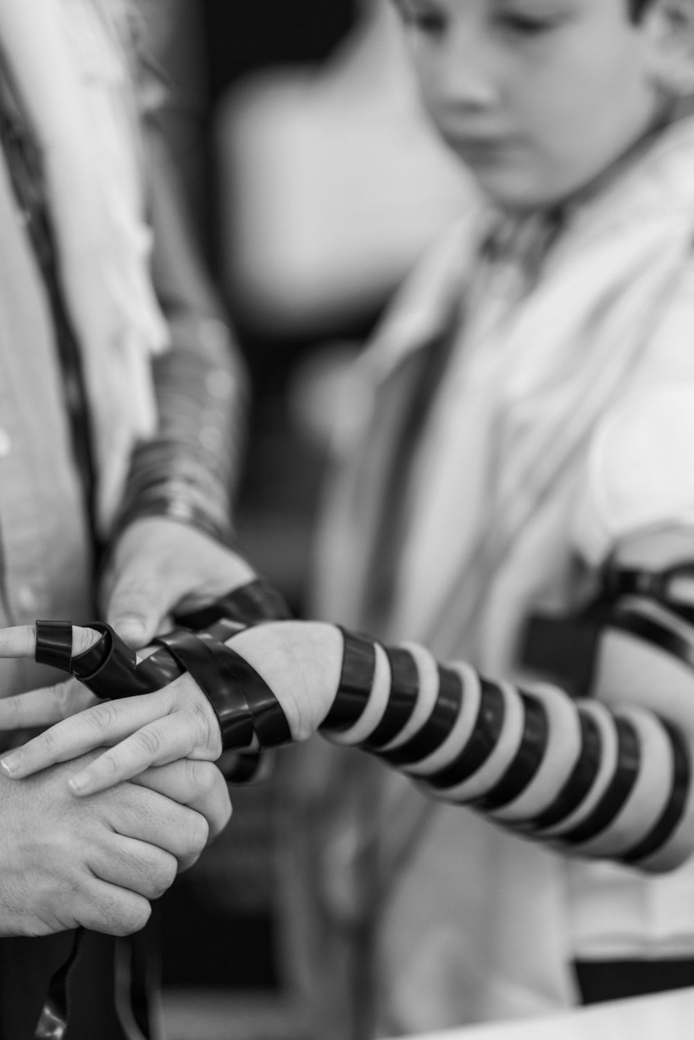 Close-up of hands wrapping tefillin straps during Jewish bar mitsva prayer ceremony.