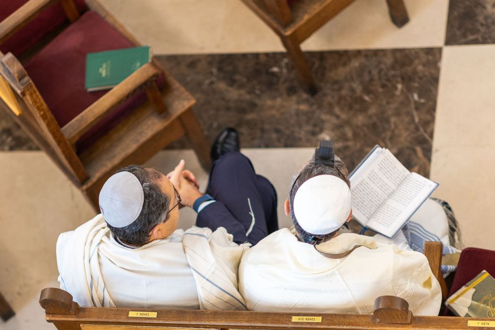 Overhead view of people studying religious texts in synagogue pews.