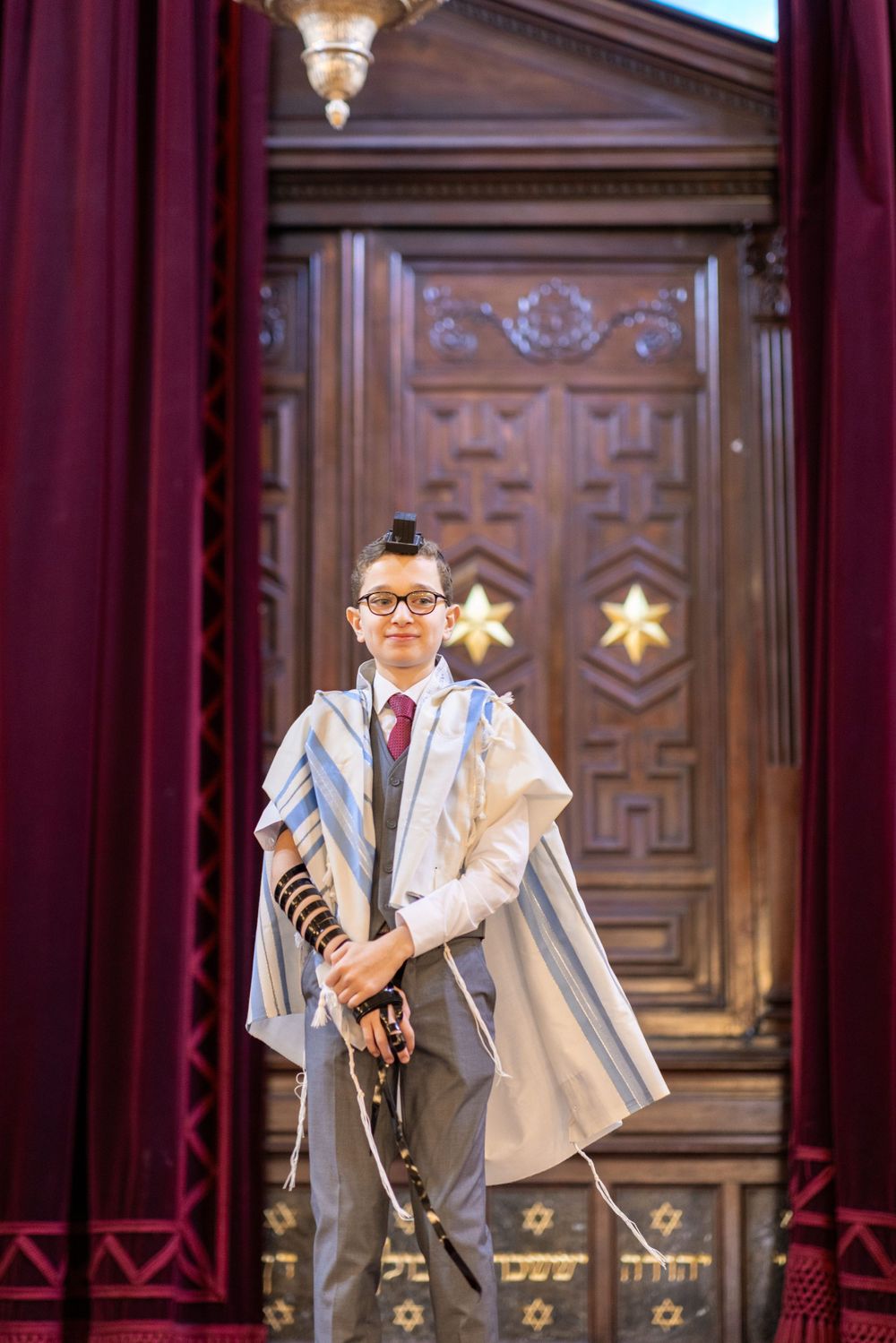 Person in formal attire holding Torah scroll in front of ornate wooden doors.