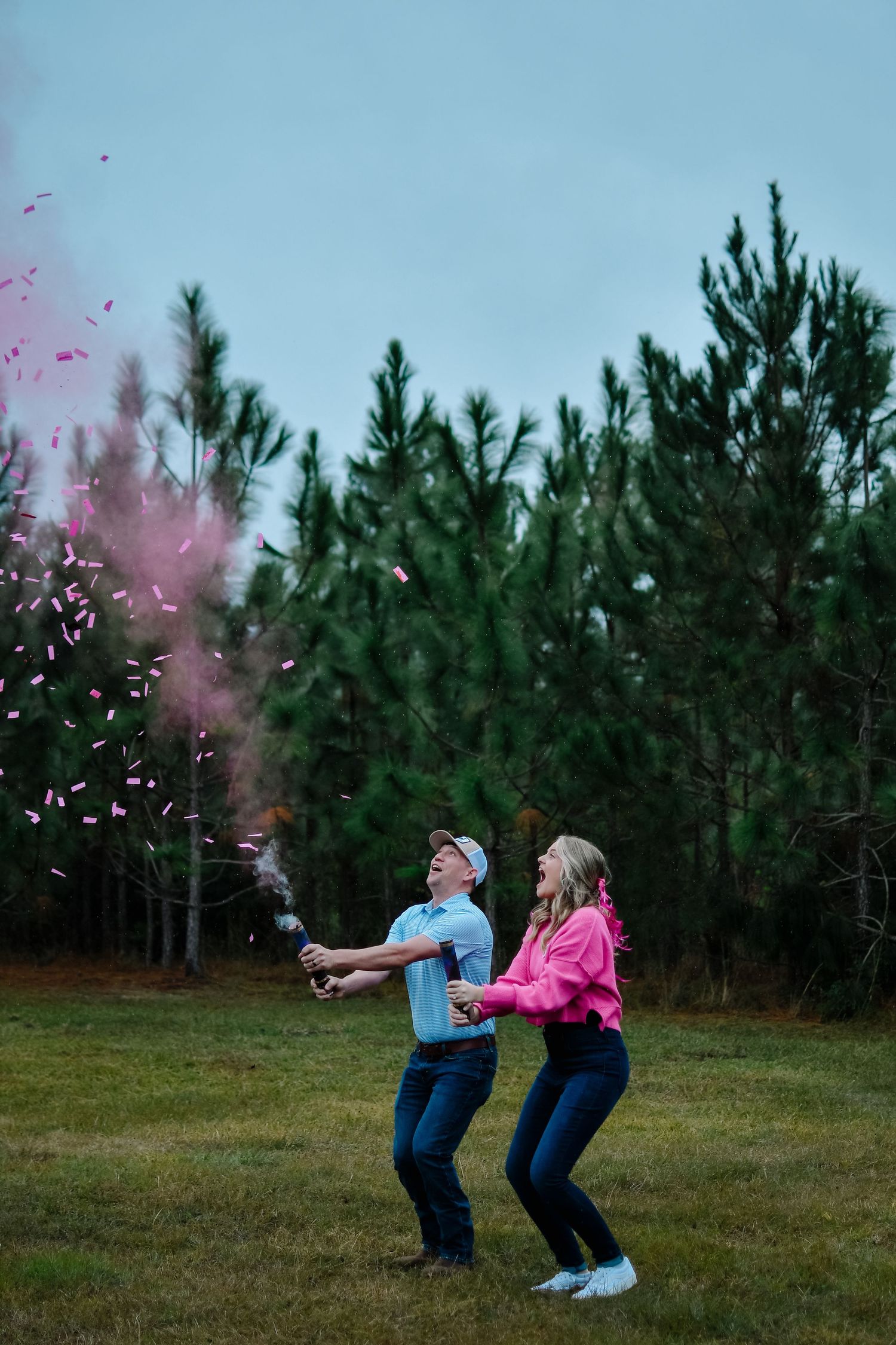 Couple celebrates with pink confetti in front of pine trees at dusk.
