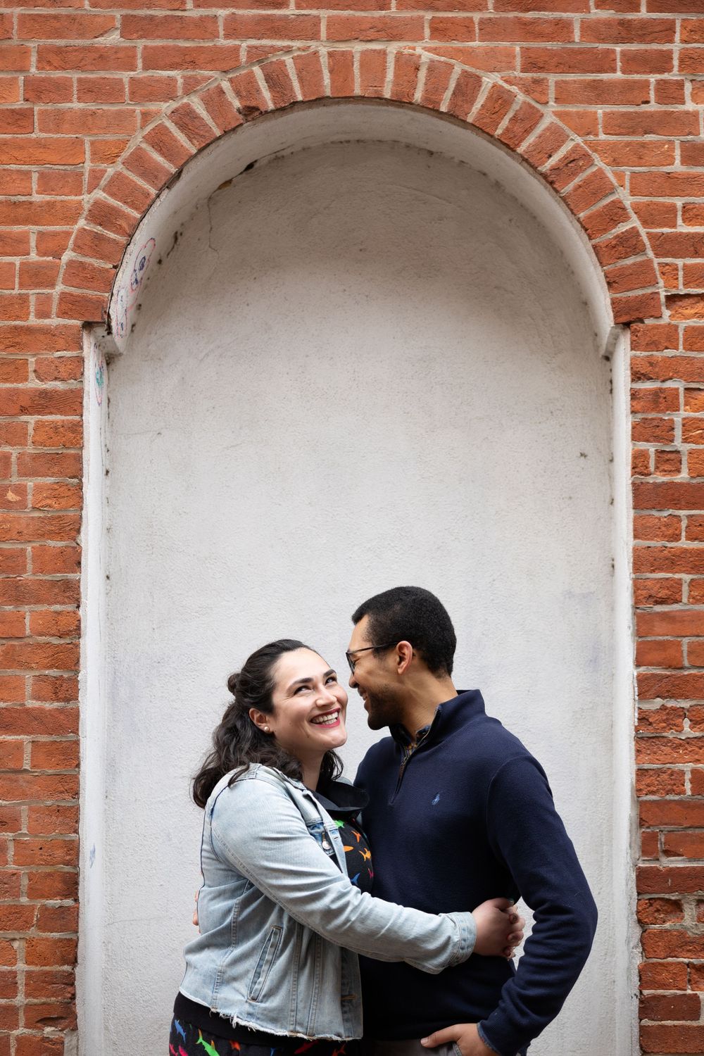 A couple embracing under a brick archway with white plaster interior.