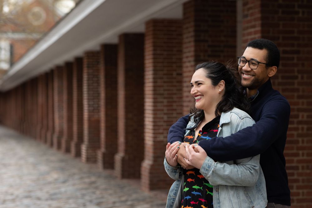 A couple shares a tender moment while embracing on a cobblestone path in front of brick columns.