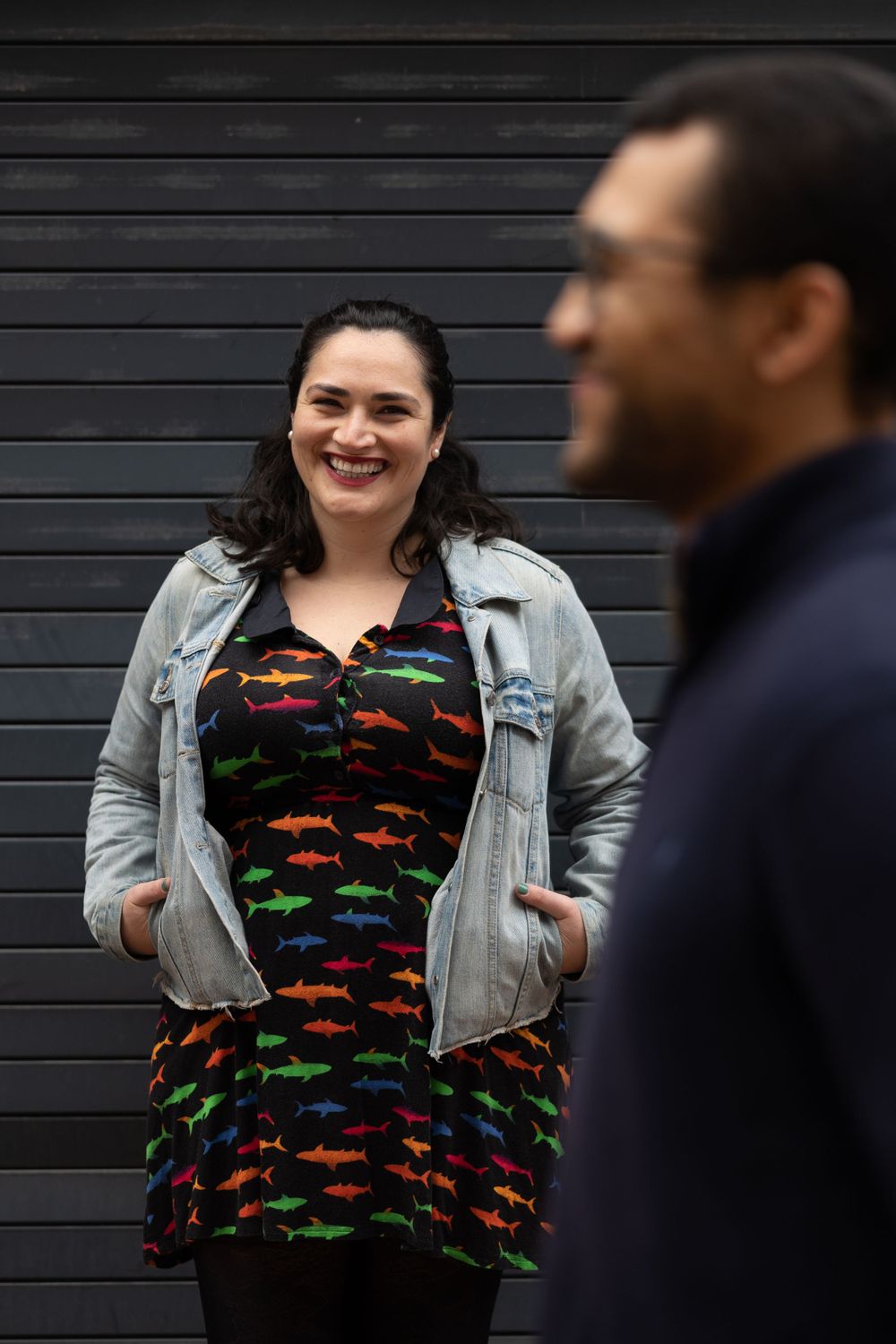 A couple in casual attire shares a joyful moment against a black wall background.