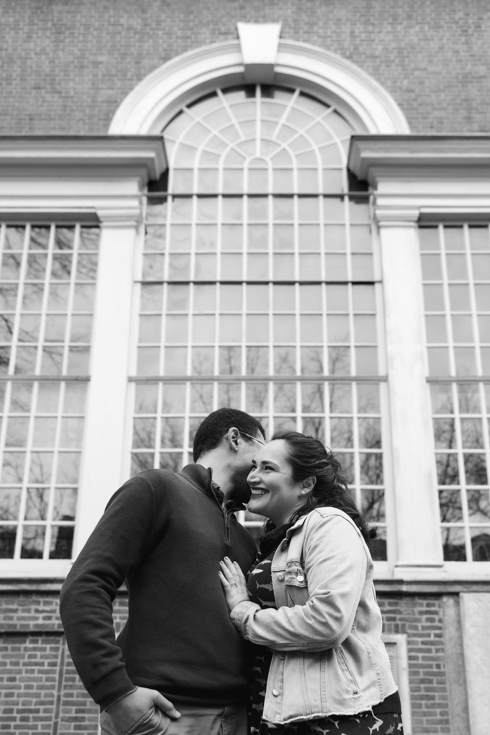A couple shares an intimate moment beneath an arched window of a historic building.