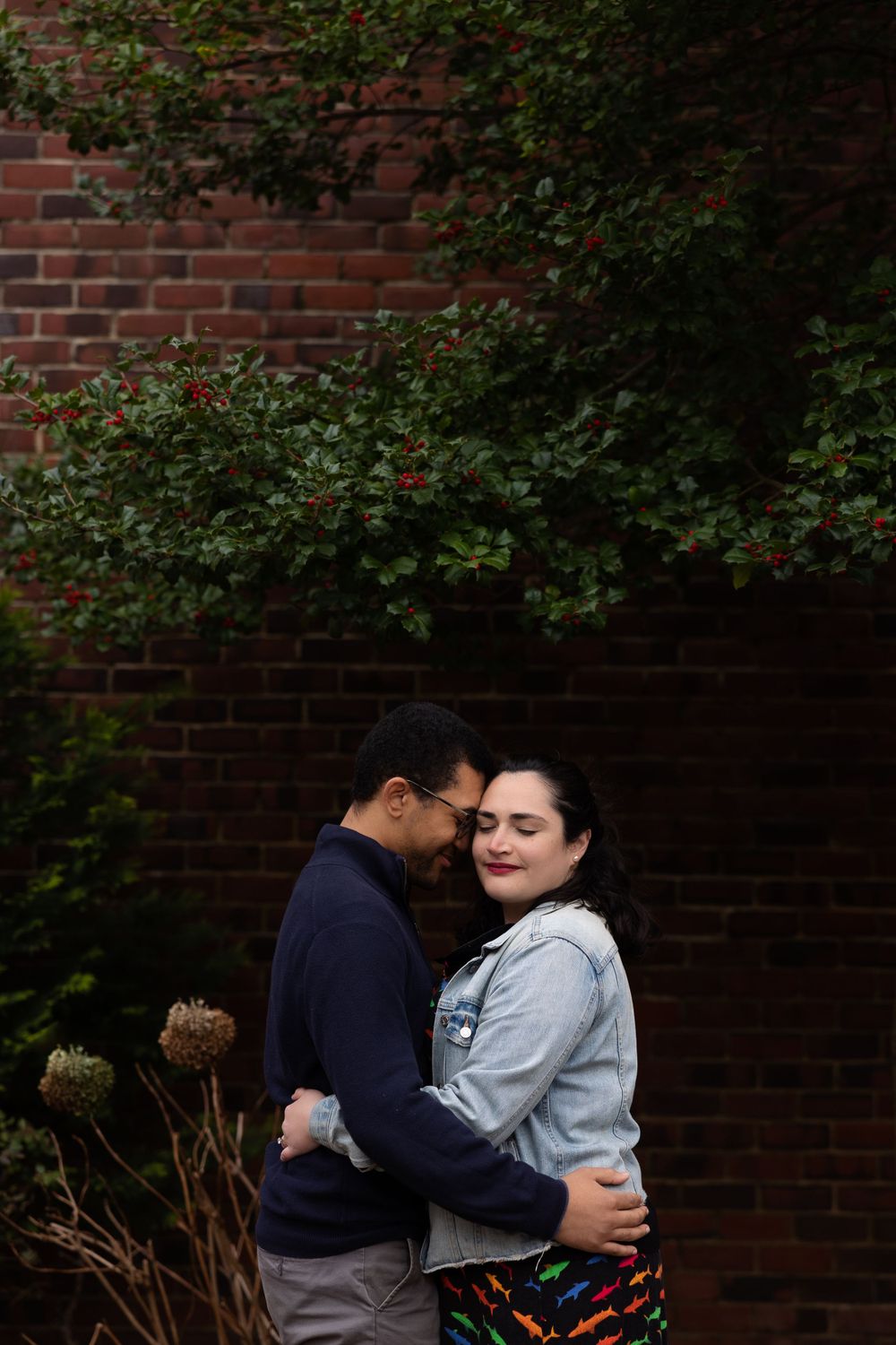 A couple shares an intimate moment among garden foliage against brick architecture.
