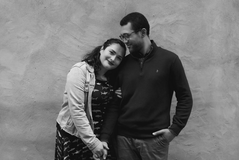 A black and white portrait of a couple sharing an intimate moment against a textured wall.