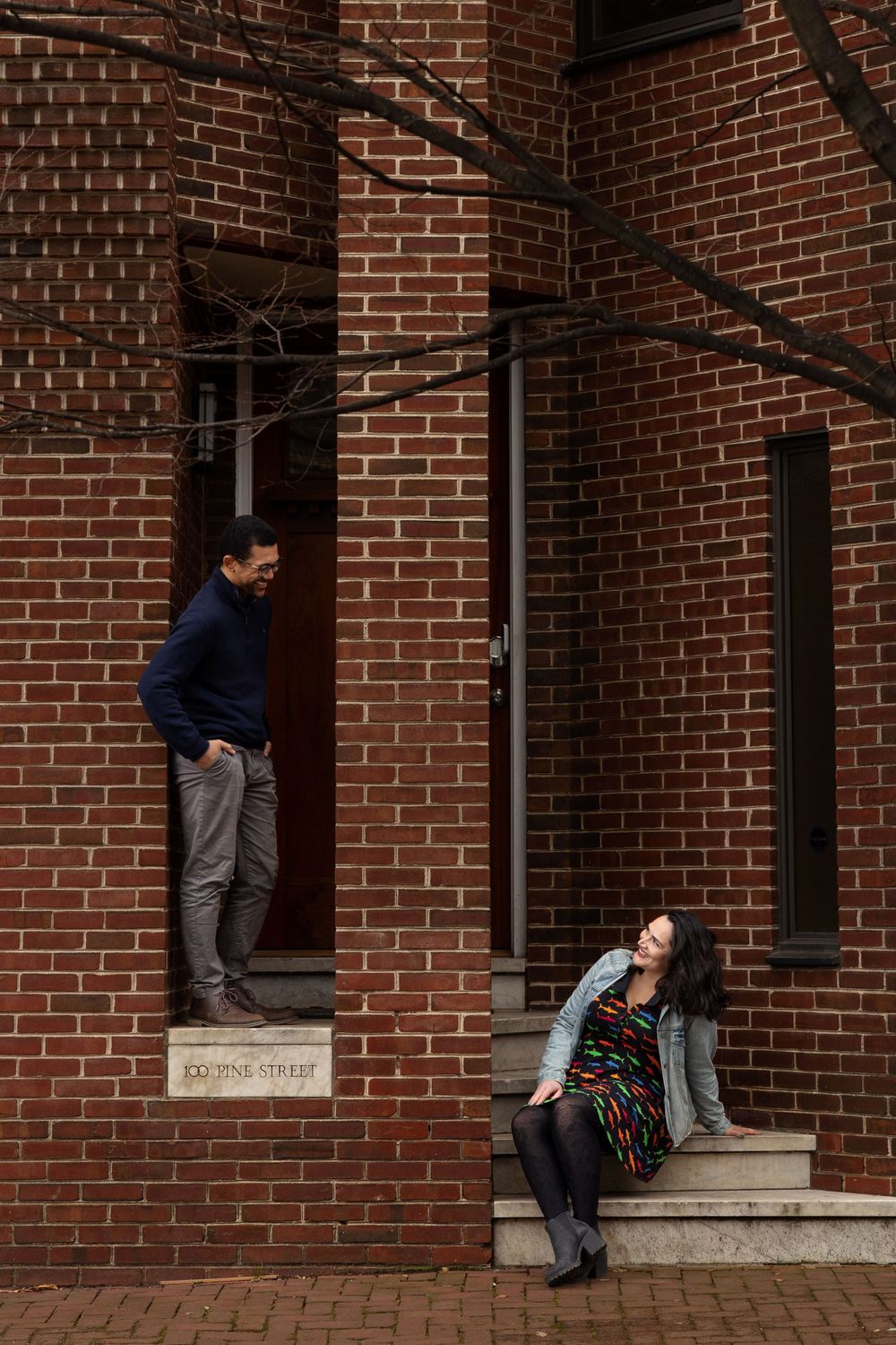 A couple poses on brick stairs in creative composition at historic building entrance.