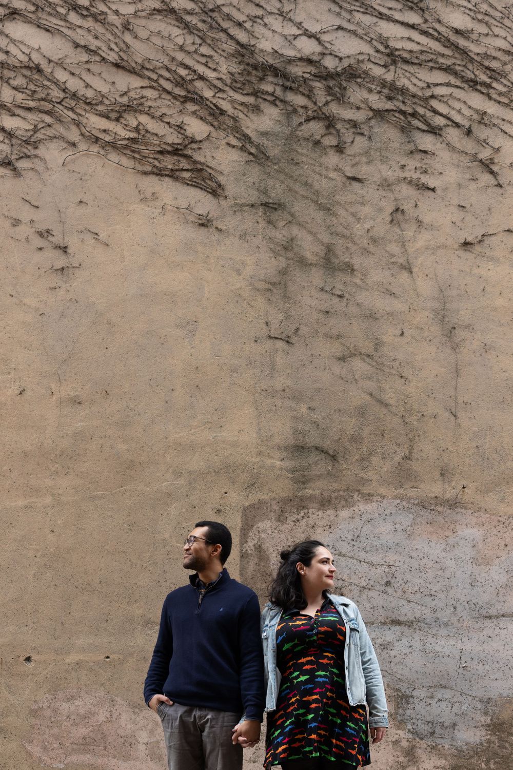 A couple standing against a textured beige wall with diagonal patterns.