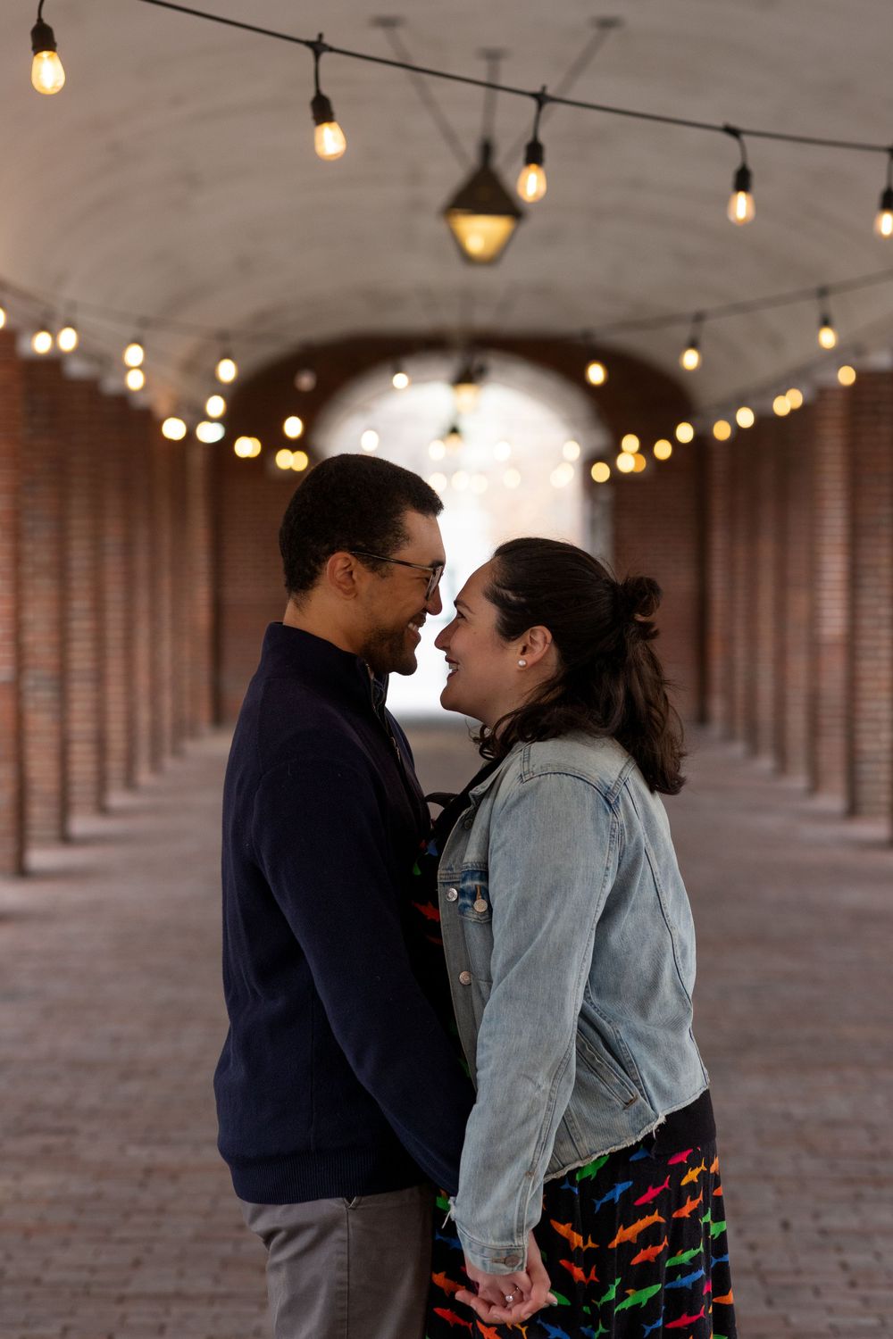 A romantic moment in a brick corridor illuminated by string lights.