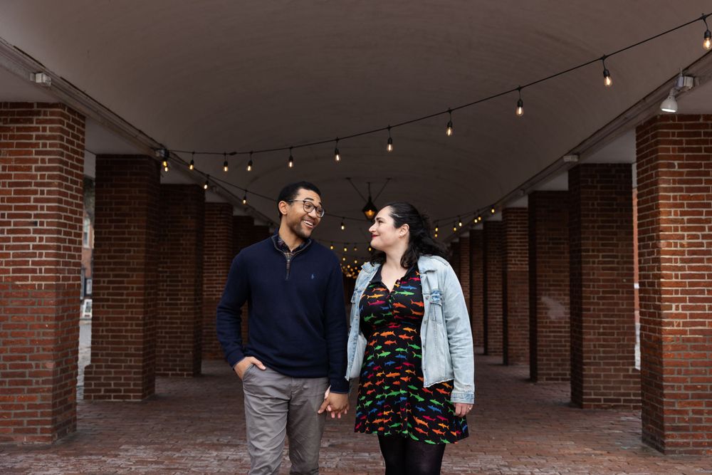 A couple sharing a laugh in a brick corridor with string lights.