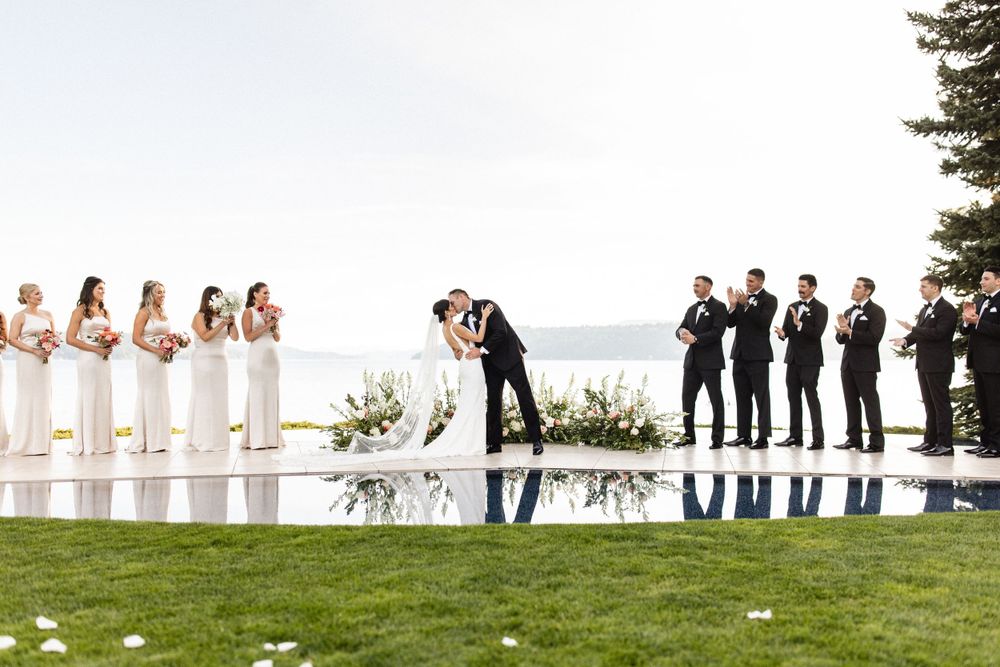 Outdoor wedding ceremony by a reflective pool with bridesmaids in white and groomsmen in black suits.