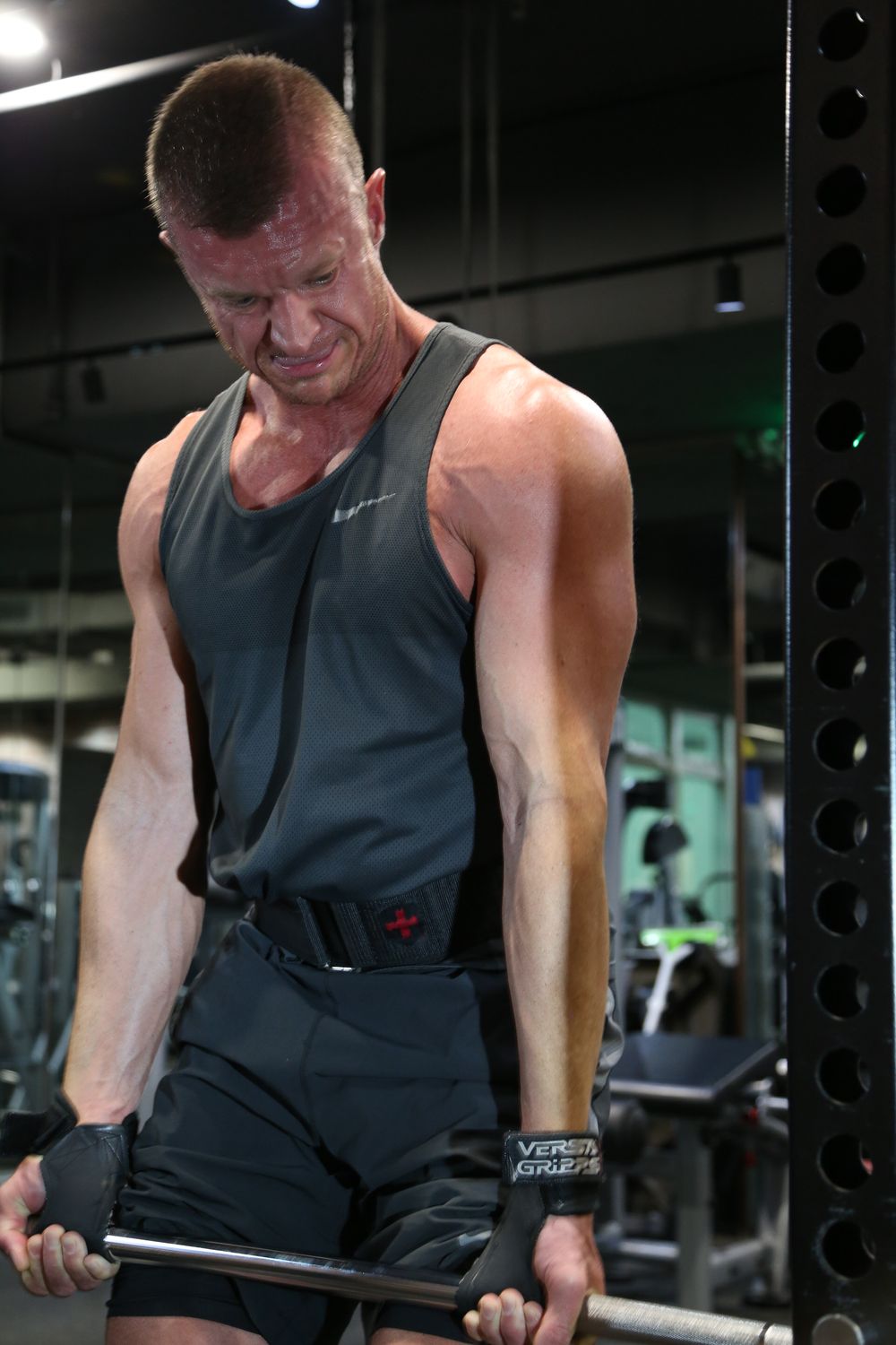 Muscular male athlete in Nike tank top performing barbell curl exercise at modern gym.