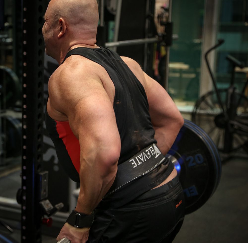 Close-up of bald powerlifter performing heavy bent-over barbell rows showing massive back muscles.