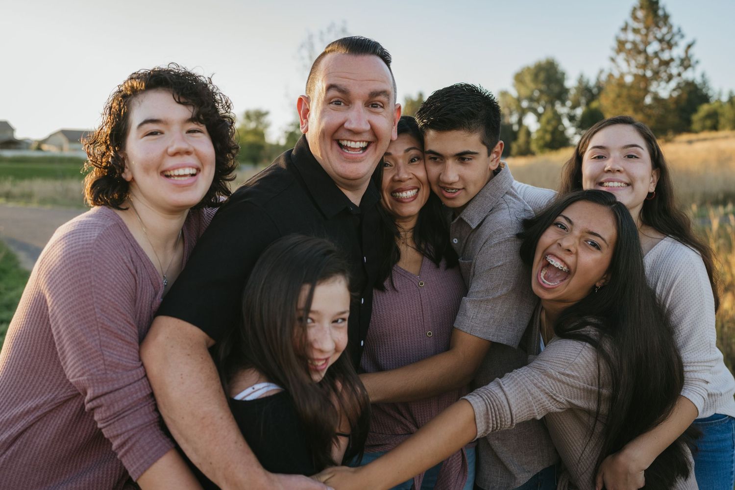 Joyful family group hugging and laughing together outdoors at sunset.