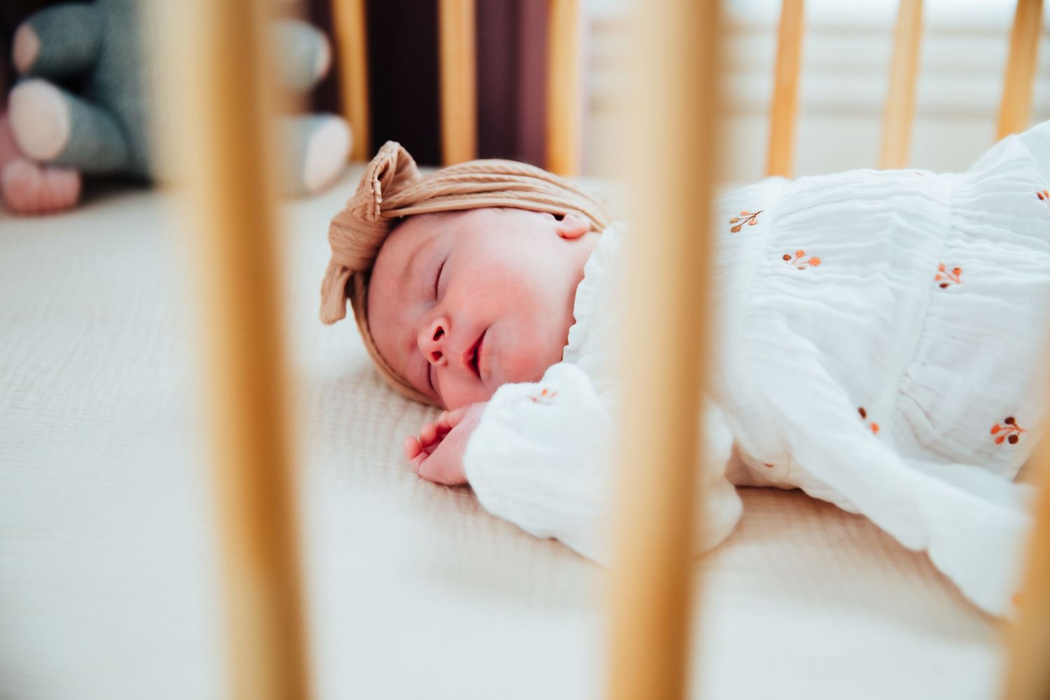 Peaceful newborn sleeping in wooden crib seen through slats.  in-home newborn photoshoot