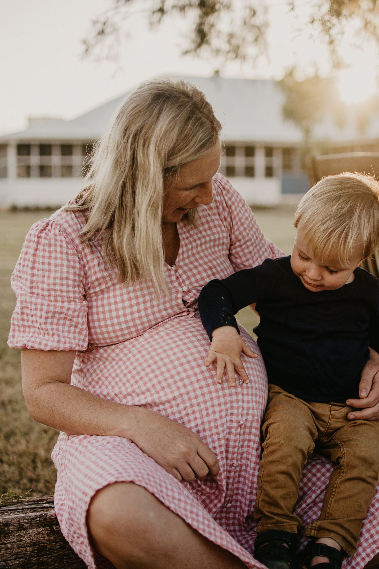 Pregnant mum sitting in the backyard at golden hour, with toddler toucher her belly