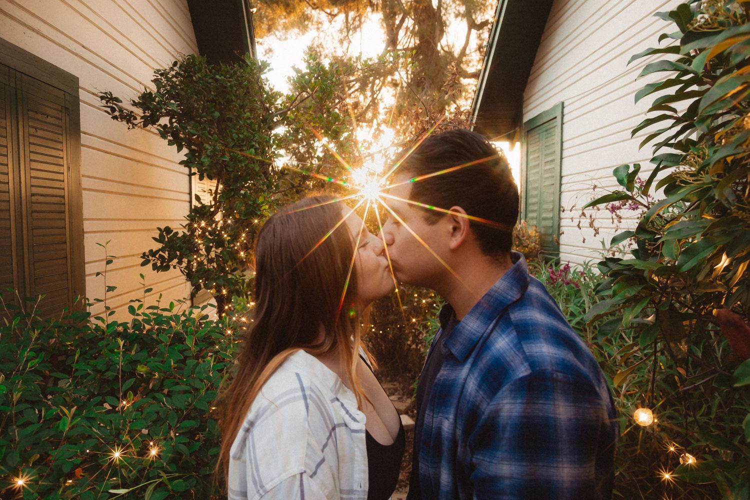 Romantic couple sharing an intimate moment in backyard with sunburst through trees.