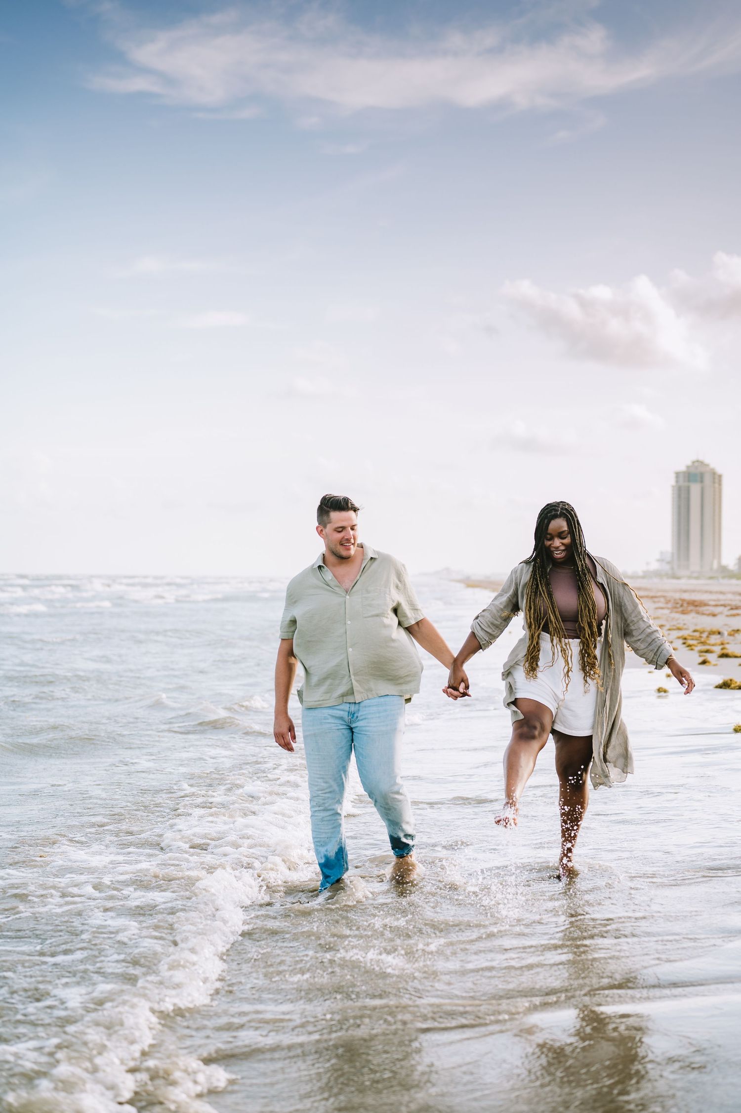 Joyful couple running and splashing through ocean waves during beach photoshoot.