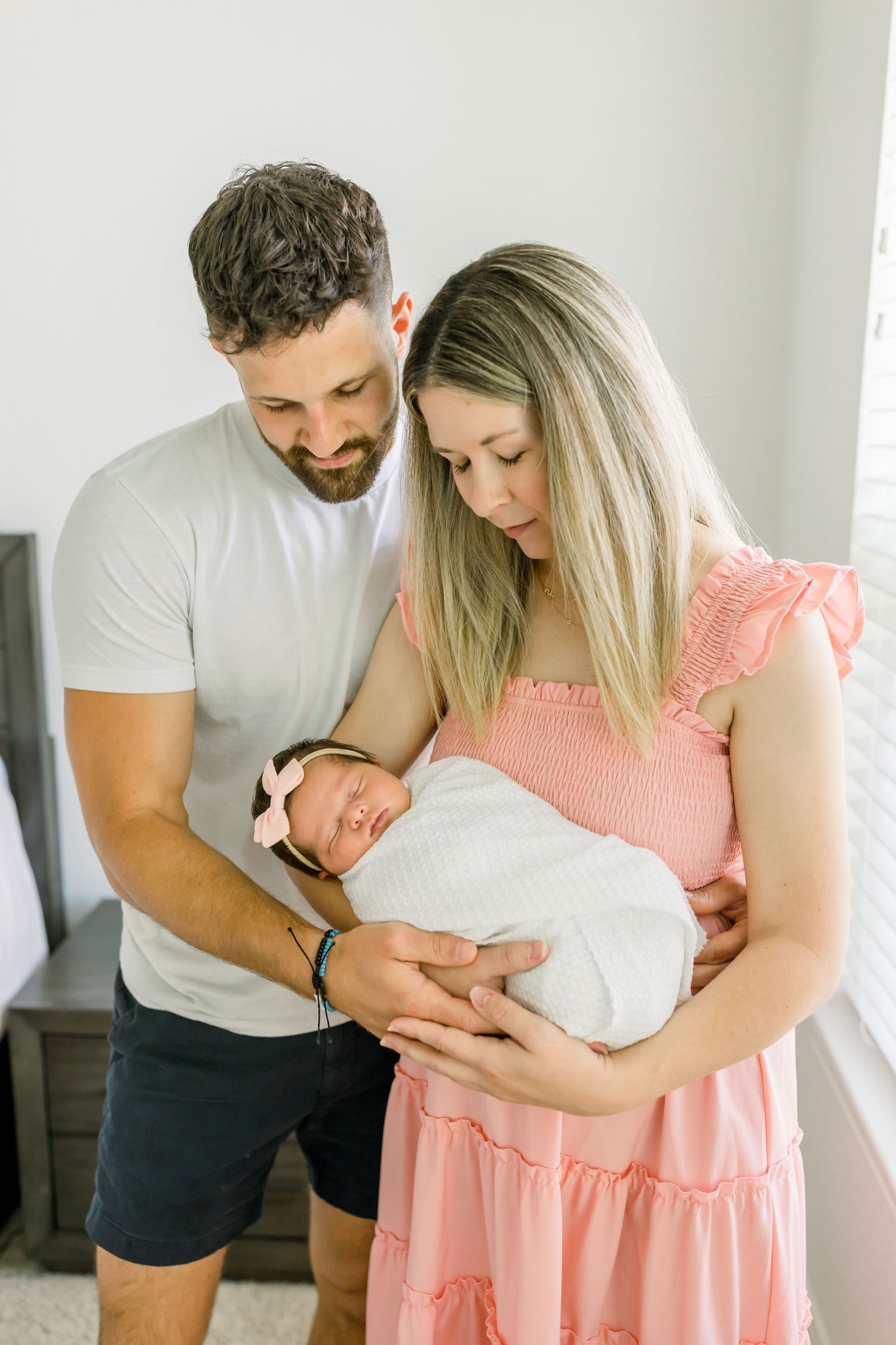 Parents gazing lovingly at their newborn baby swaddled in white.