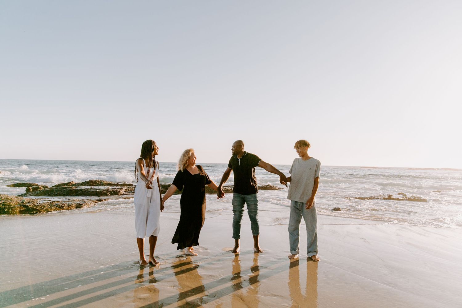Family walking together on a scenic beach at sunset with waves and sand in the background.