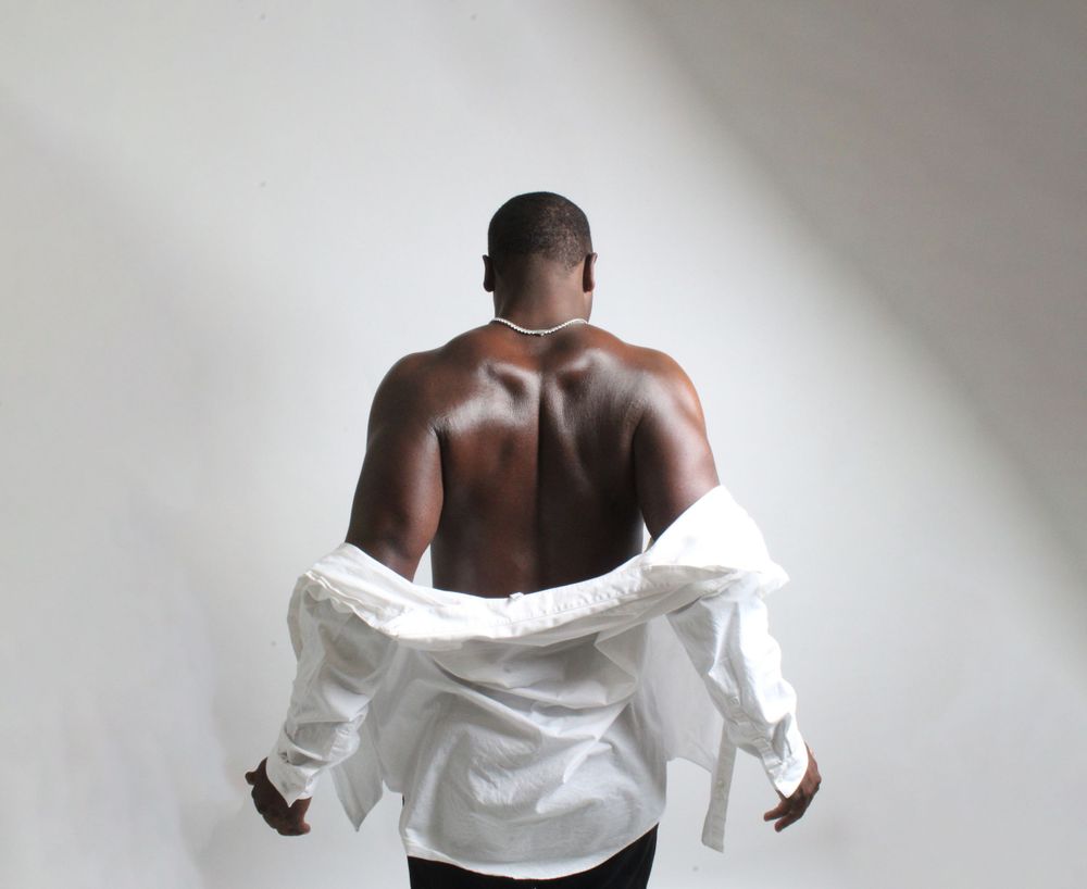 Back view of model wearing partially removed white shirt against minimalist background.