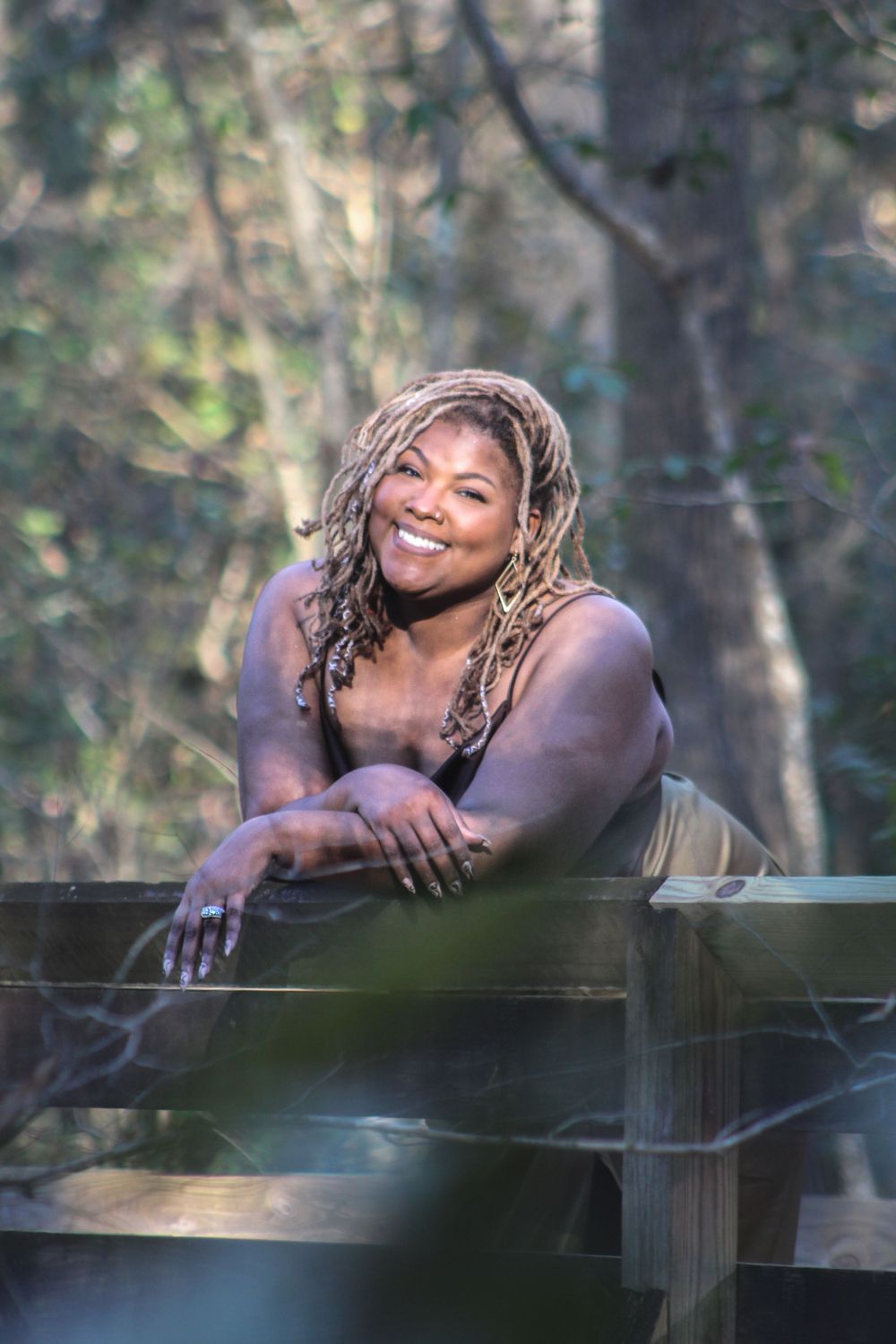 Outdoor portrait at wooden railing with natural bokeh background.