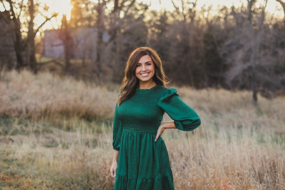 Woman in emerald green dress poses in field during golden hour.