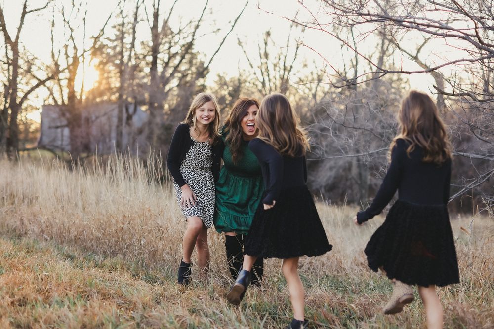 People running and laughing together through tall grass at sunset.