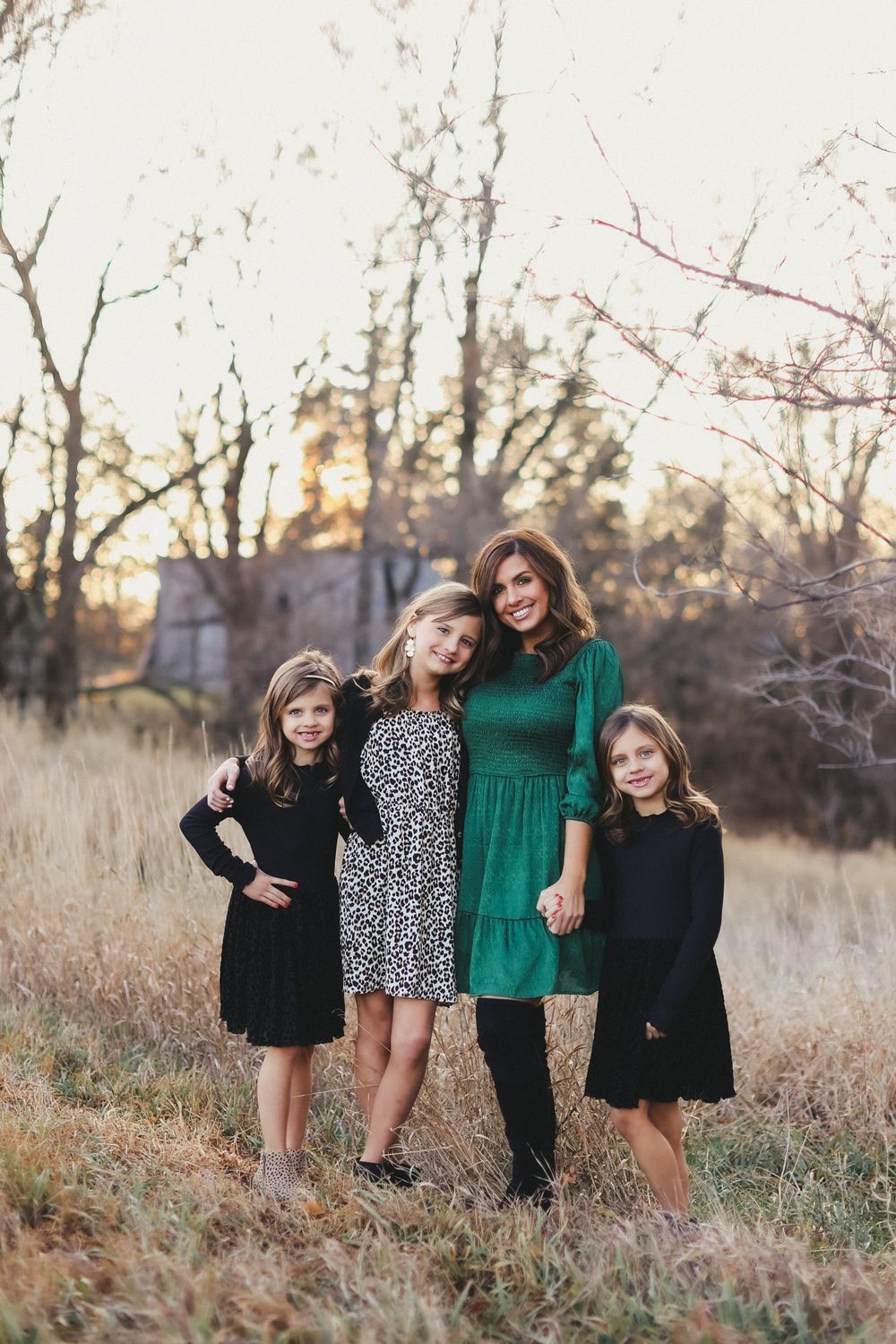 Family portrait in coordinated outfits standing in autumn field at sunset.