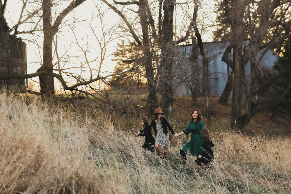 People walking through golden grass field with bare trees at sunset.
